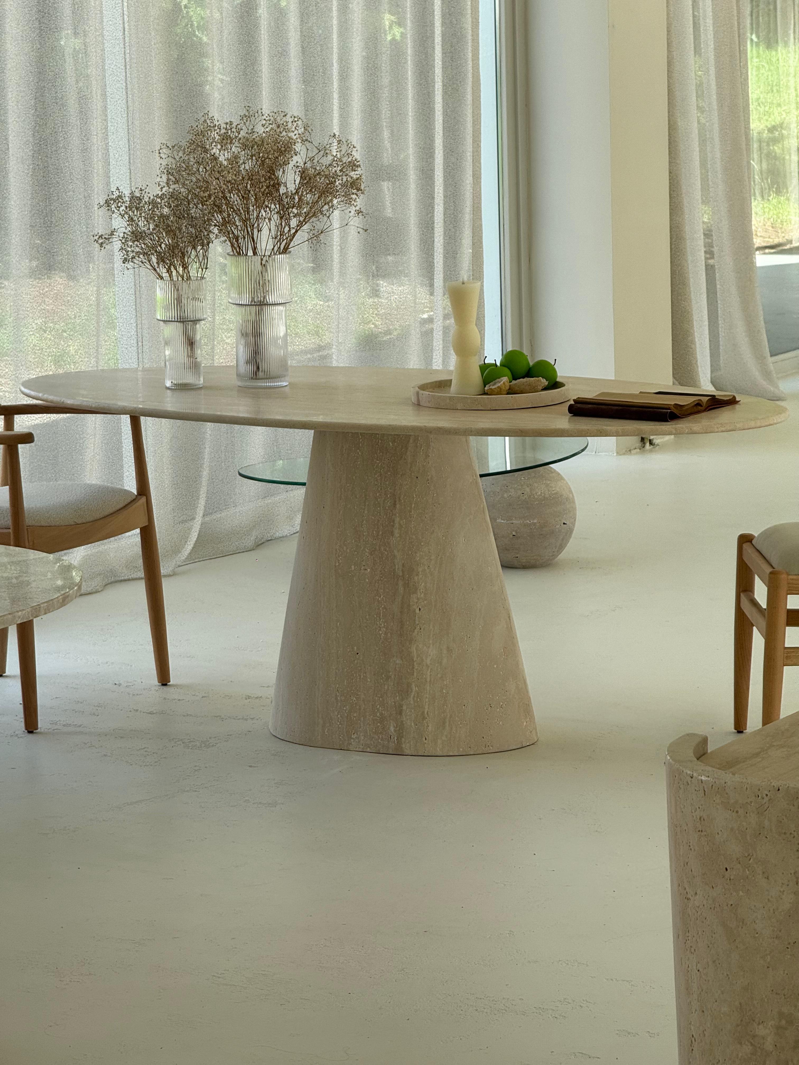 Close-up of the Cammilia Travertine Ellips Dining Table with elliptical top and conical base in natural honed stone finish