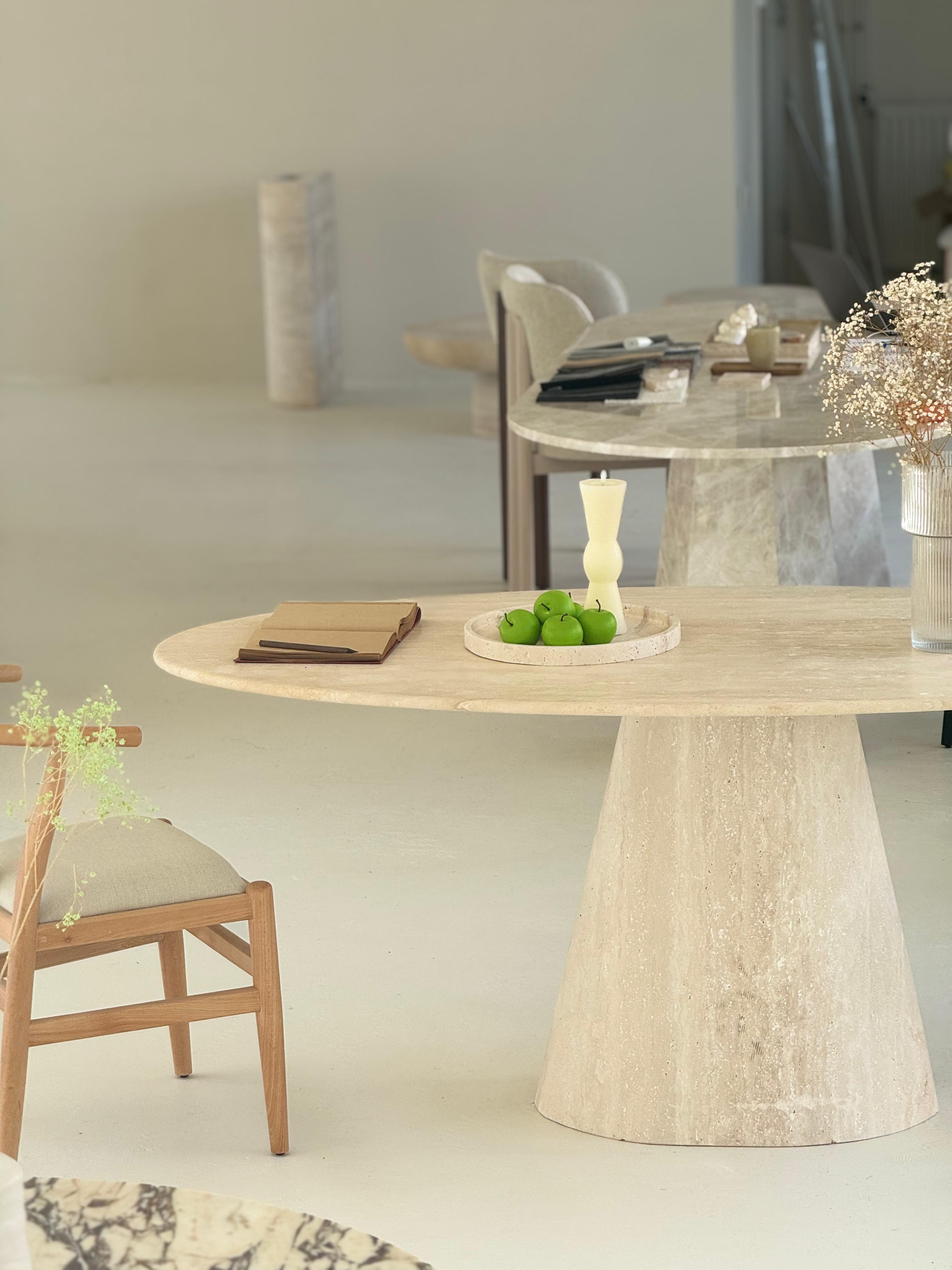 Close-up of the Cammilia Travertine Ellips Dining Table with elliptical top and conical base in natural honed stone finish
