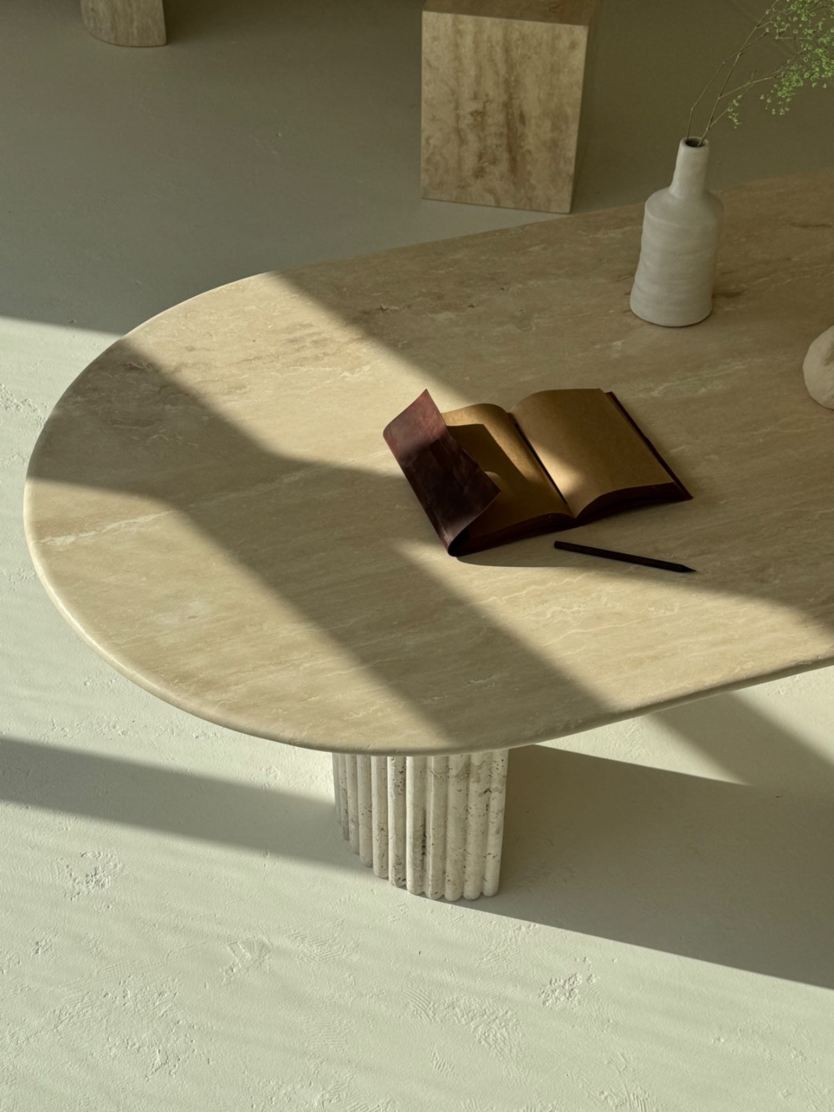 Travertine oval dining table Bambusa with vein cut top and spider base in daylight interior