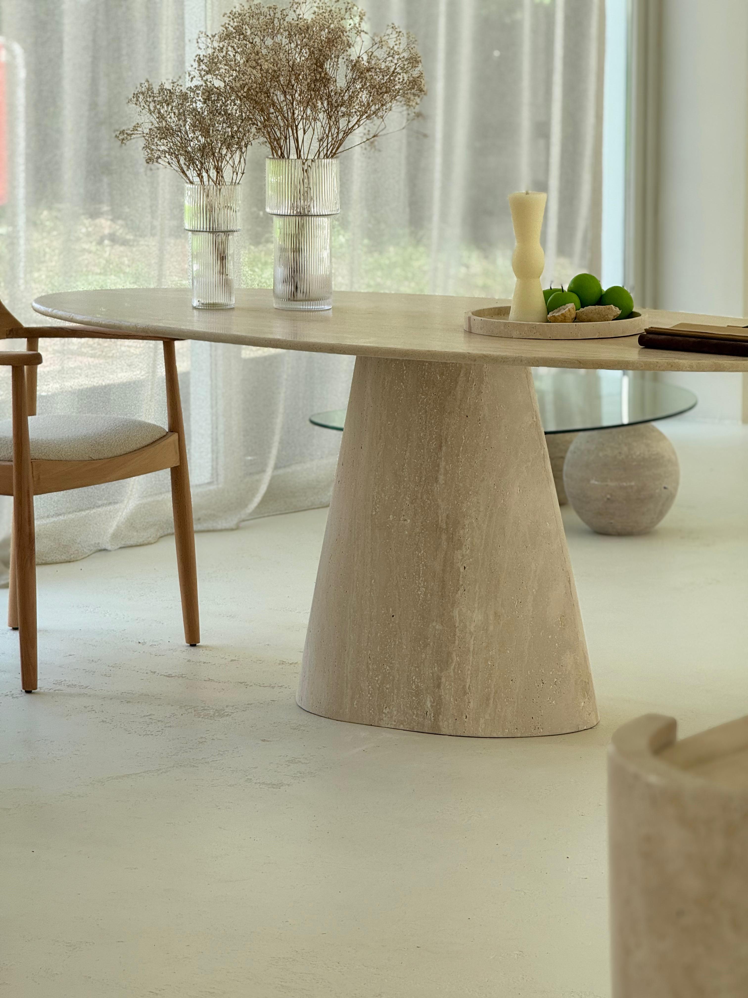Close-up of the Cammilia Travertine Ellips Dining Table with elliptical top and conical base in natural honed stone finish