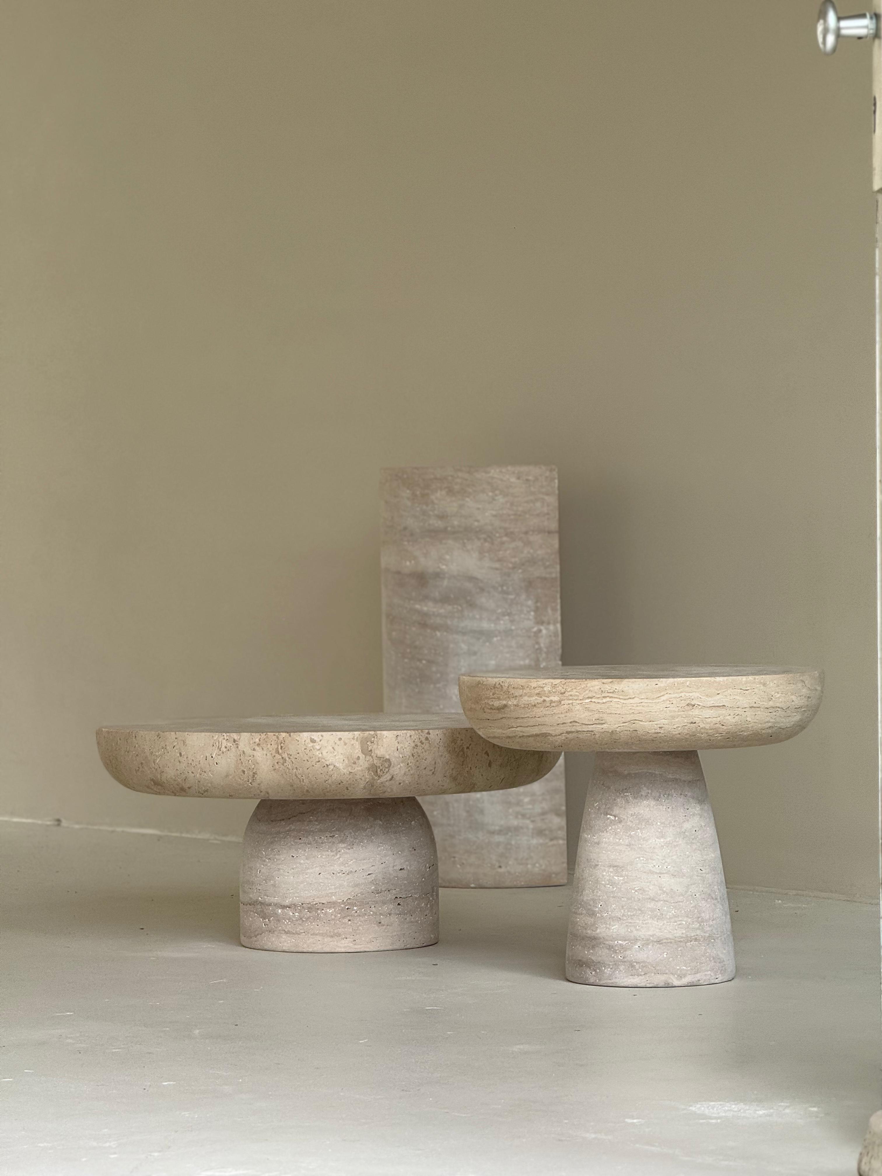 Set of two round travertine coffee tables with sculptural bases and polished stone tops in beige tones, styled in a modern neutral living room.
